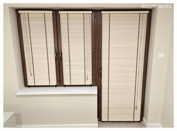 Drewniane żaluzje w kremowym kolorze z dekoracyjną brązową taśmą podkreślają naturalny charakter i ciepło pomieszczenia.