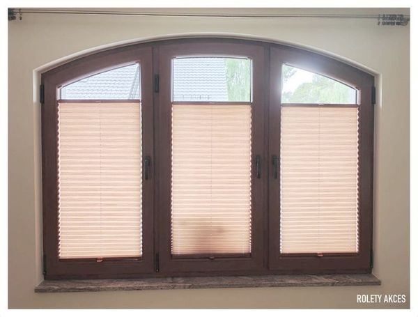 Beżowe plisy zamontowane na łukowych oknach z okleiną w kolorze orzecha